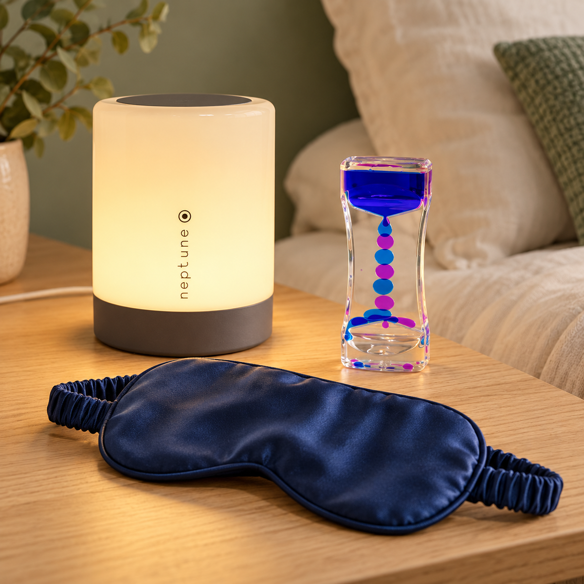 Sleep lamp, colourful liquid timer and navy silk sleep mask on a bedside table
